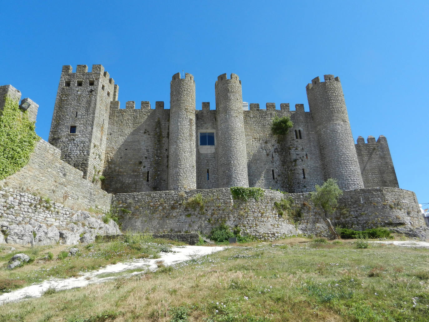 Castillo de Óbidos (Portugal). La construcción de este castillo mágico se remonta a la presencia romana en Portugal. El castillo de Óbidos tiene torres en forma de cilindro y cuadradas, mientras que la piedra caliza y el mármol añaden una faceta grandiosa a la fachada. Es un buen ejemplo de una fortificación bien conservada, y el castillo ha escapado al destino de ser convertido en ruinas, y se ha transformado, según Jetcost.es en uno de los hoteles pequeños más románticos de Portugal. El pueblo que lo rodea, Óbidos, es conocido por sus atractivos paisajes y exuberante vegetación. El que una vez ofreció protección militar en el corazón de Portugal, ahora ofrece como hotel a los visitantes la oportunidad de viajar en el tiempo, según la web Jetcost.es