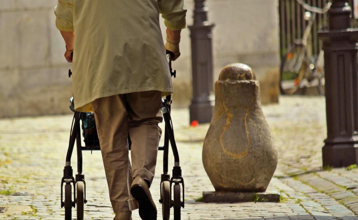 Una persona mayor camina por la calle con ayuda de un andador. 
