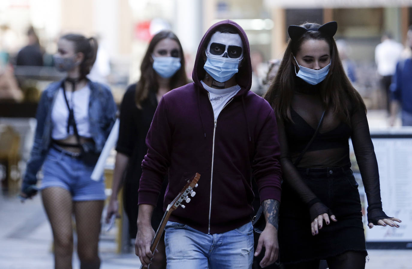 Personas disfrazadas se mezclan con las que llevan mascarillas en un paso de peatones en Málaga capital.
