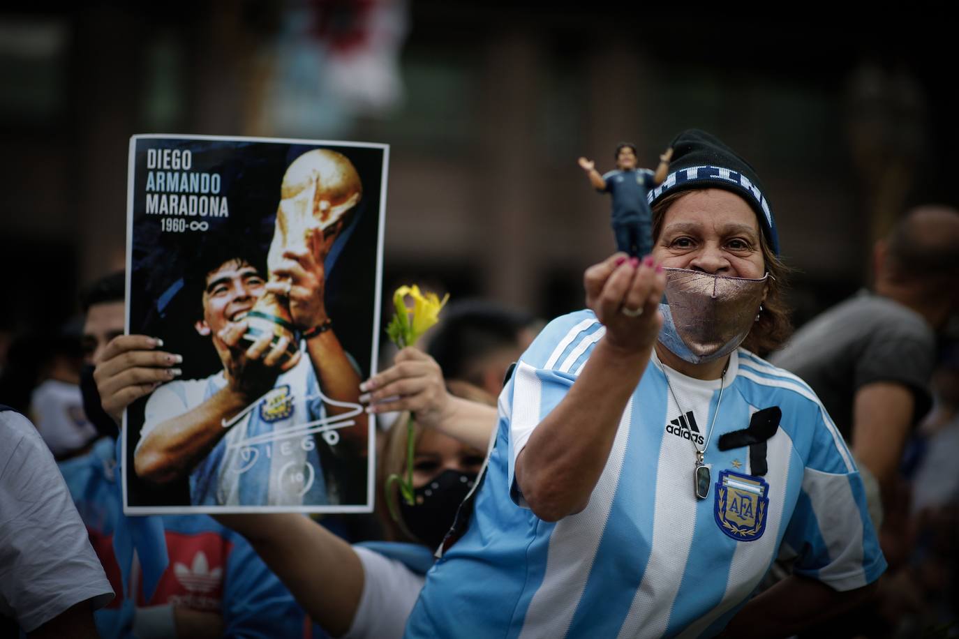 Una imagen de Maradona con la Copa del Mundo de 1986 y una mujer con una imagen del '10' argentino.