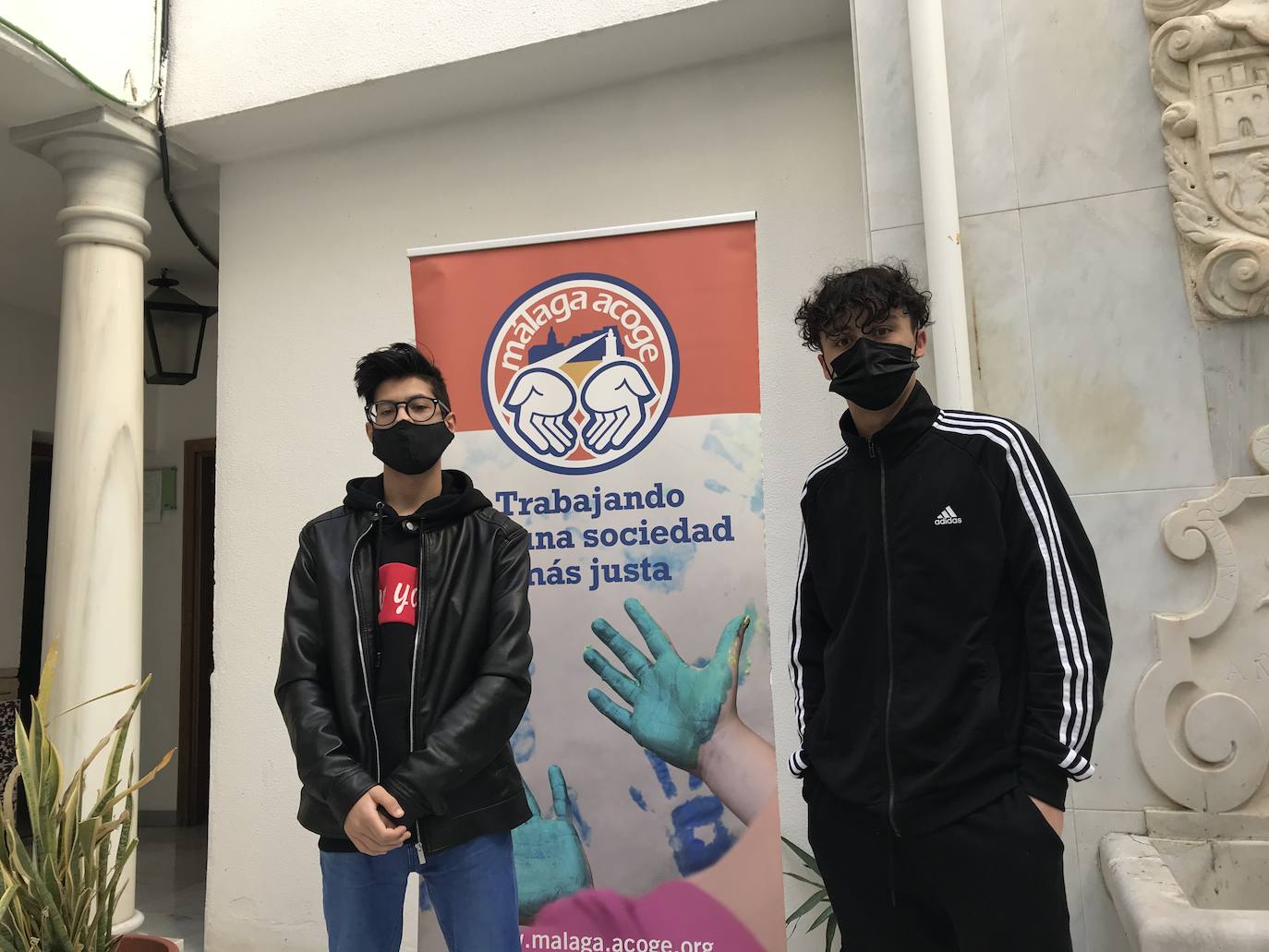 Ayman y Hassan, posan delante de un cartel de Málaga Acoge. 