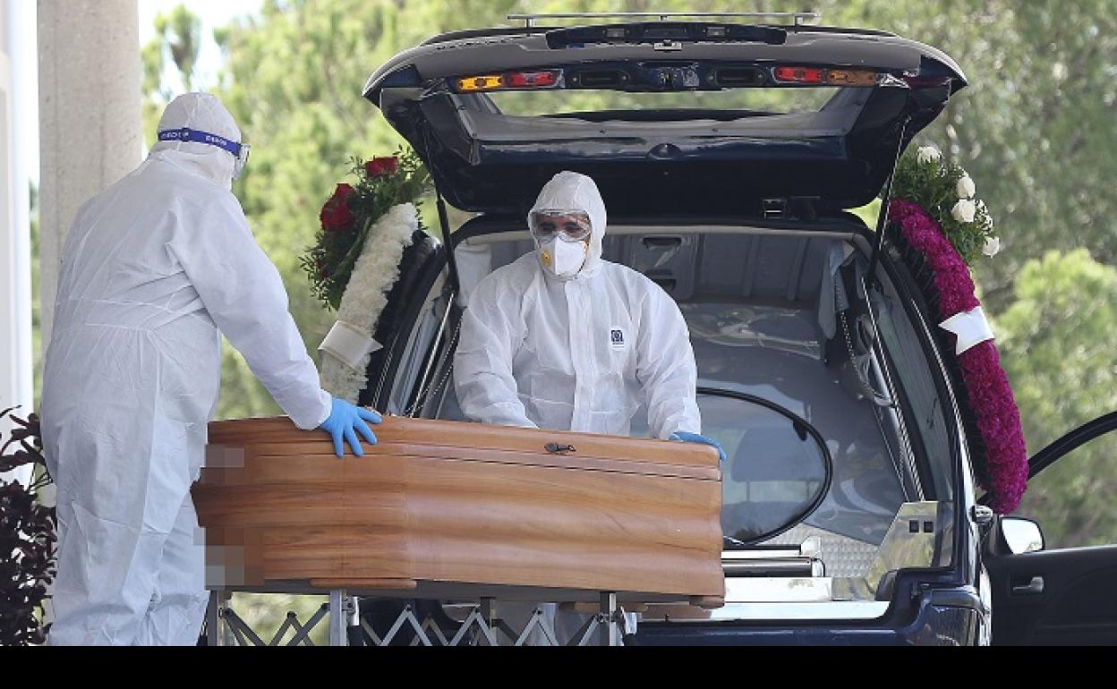 Dos trabajadores de introducen el féretro de un fallecido por coronavirus en el coche fúnebre. 