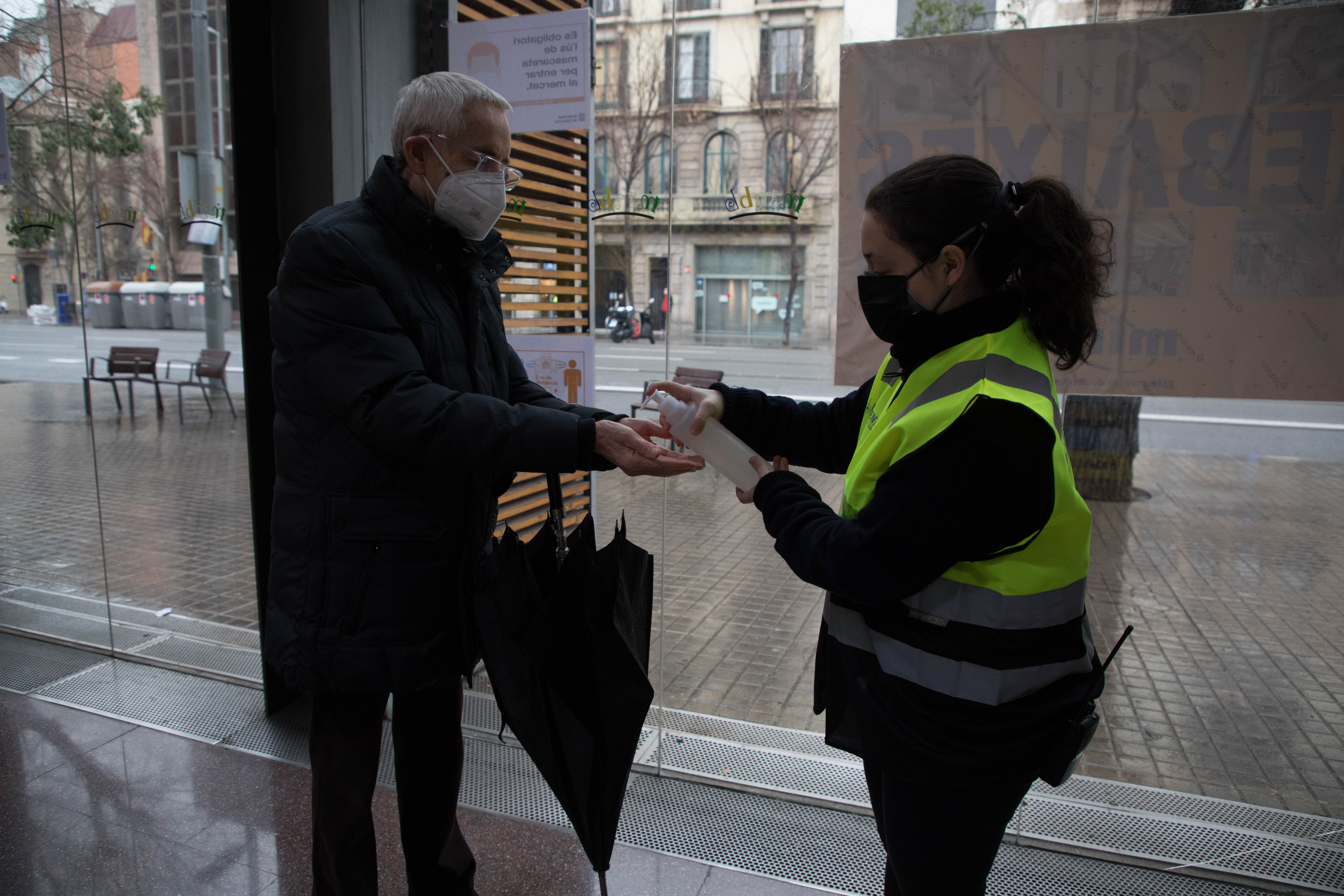 Una persona de seguridad facilita gel hidroalcohólico a una persona que se acerca a votar en el mercado de la Concepciò.