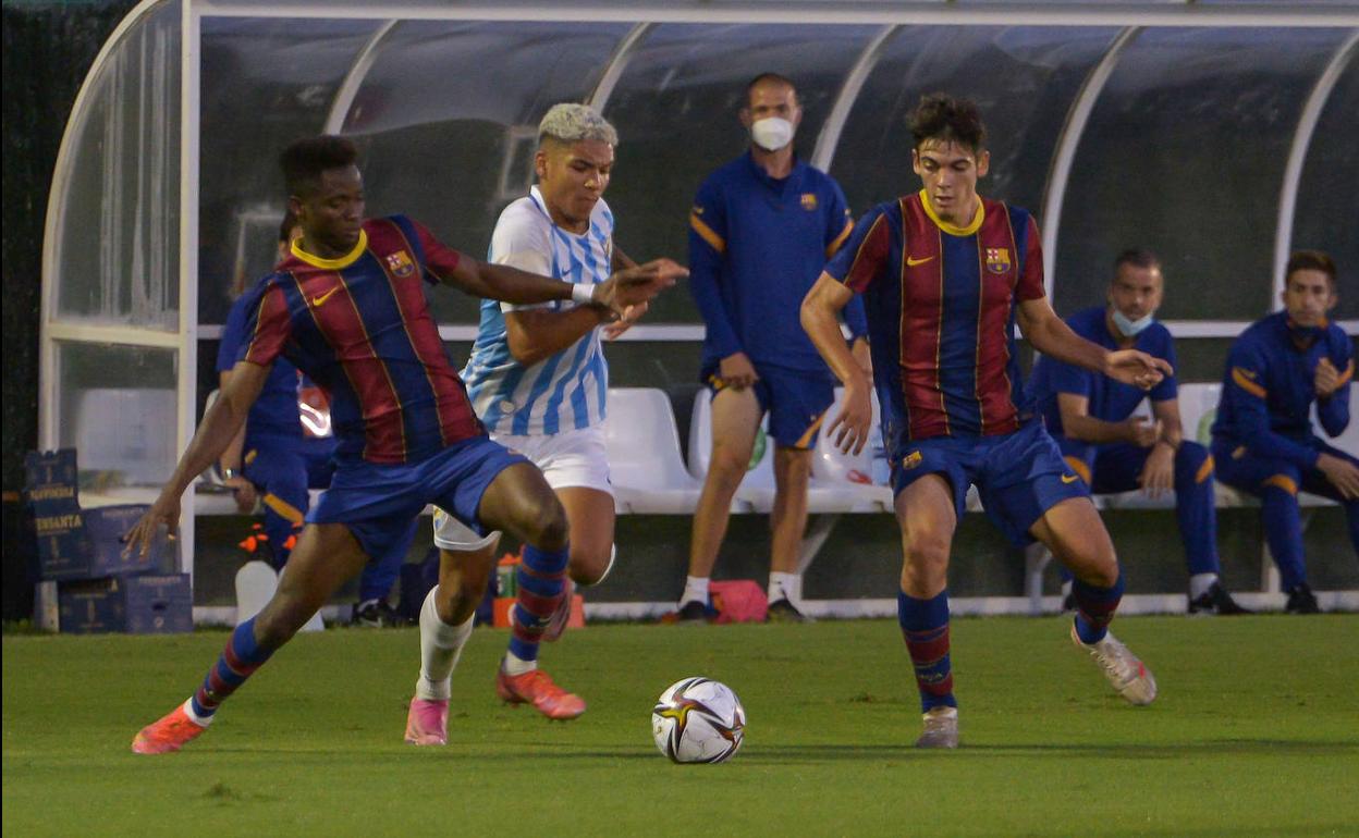 El delantero del Málaga, Loren Zuñiga, intenta hacerse con el balón frente a dos defensas del F.C. Barcelona.
