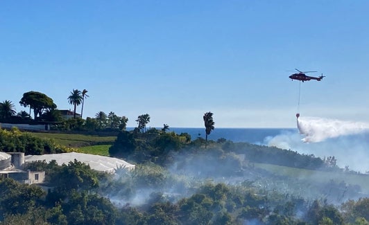 Un helicóptero sofocando las llamas junto a la pedanía al mediodía de ayer. 
