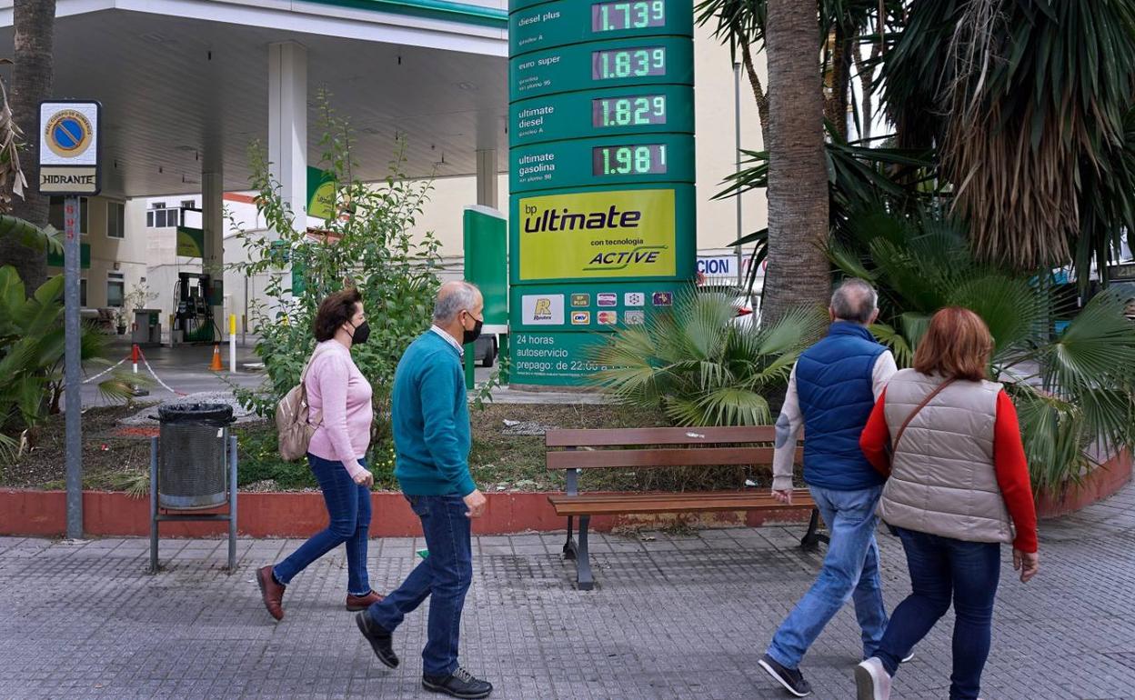 Un grupo de personas pasan delante de una gasolinera donde se exhiben los precios de los carburantes. 