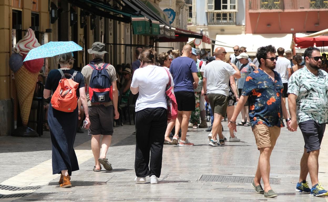 Turistas pasean por el Centro de Málaga ataviados con gorros e incluso sombrillas frente al calor. 