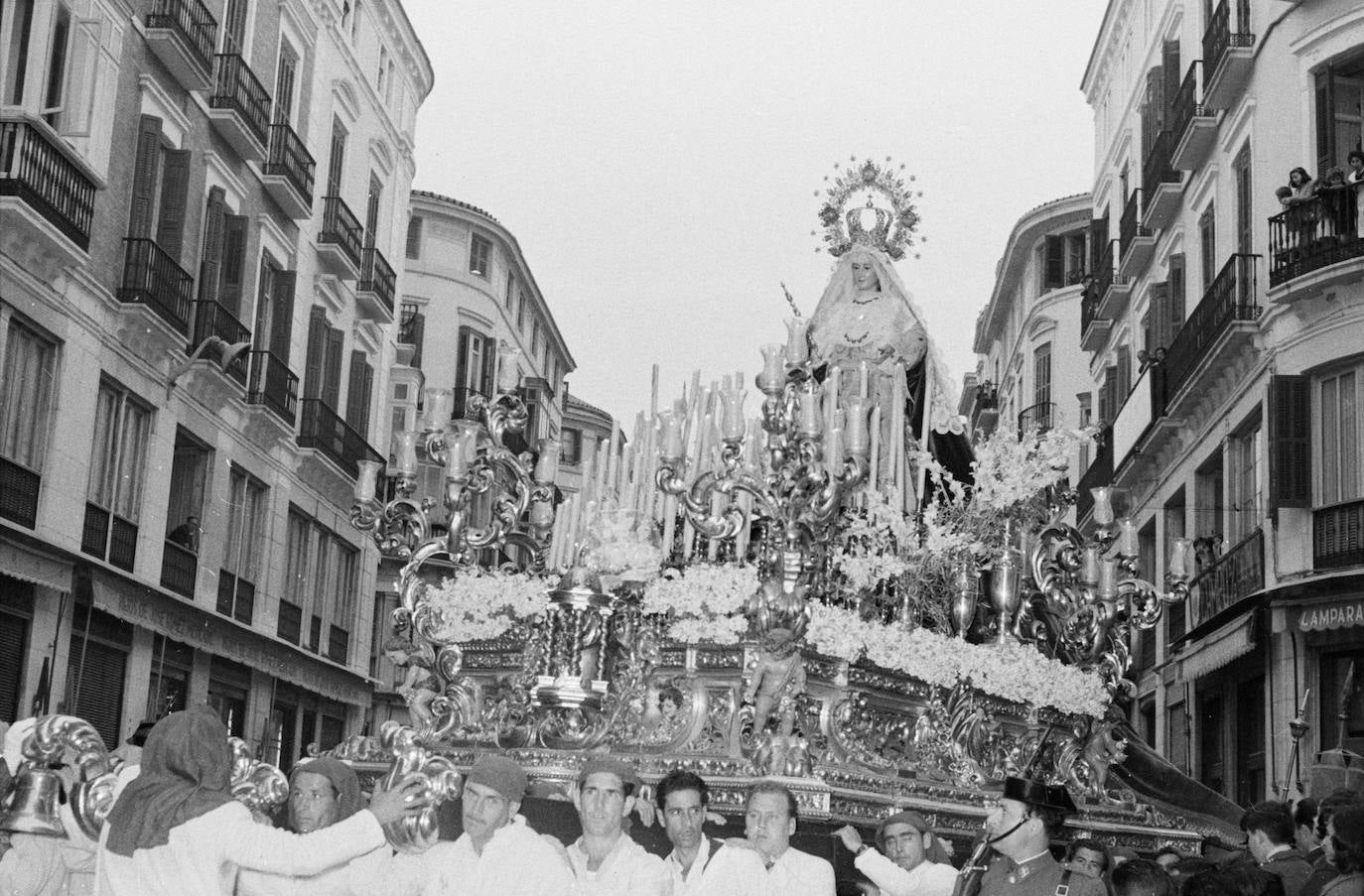 Es el año 1959. El trono de madera dorada que Antonio Castillo Ariza hizo para la Virgen del Amparo que talló en 1947 para la Cofradía de la Pollinica cruza la calle Larios. La imagen porta en su mano un cetro, lo que refuerza su carácter glorioso o letífico.