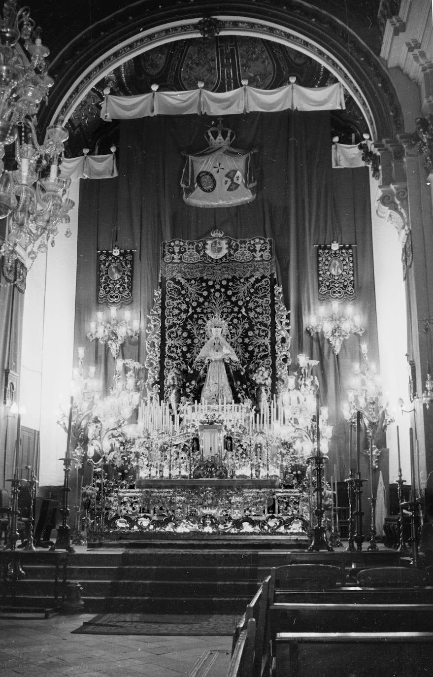 El altar mayor del templo de San Juan acogía la celebración de los cultos de la Virgen de la Paloma. Como se aprecia en esta fotografía de 1959, los hermanos no escatimaban a la hora de instalar el altar. Incluso, utilizaban elementos del trono, como el palio y los arbotantes.