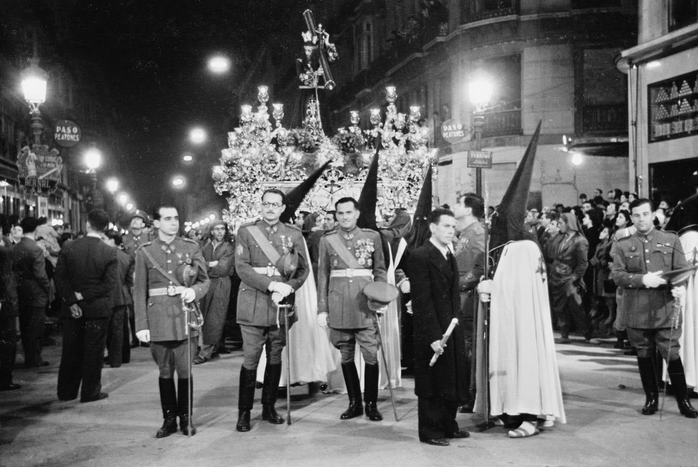 El trono de Jesús El Rico, obra de Nicolás Prados López, en 1942, detenido en su desfile procesional por la calle Larios. En la imagen se observa a un hombre, que vestido con un largo abrigo oscuro, acompaña a la presidencia del trono portando una vela encendida. Es el penado que fue liberado ese año por la imagen del Cristo, cumpliéndola secular tradición asociada a esta cofradía.