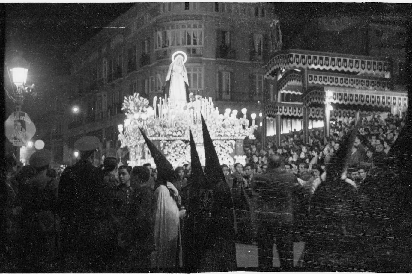 La Virgen del Gran Poder, ante la tribuna principal de la hoy plaza de la Constitución. Destacan los enormes doseles que coronaban las gradas del público. El trono fue realizado por los malagueños José Castro García y Enrique Guerrero Utrera en 1941. La imagen luce sin palio y con un llamativo aro dotado con iluminación eléctrica.