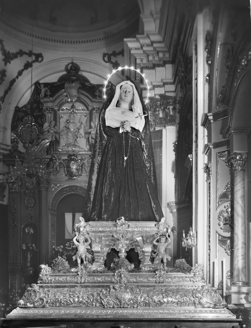 Tras su paso por la parroquia de los Mártires, la Virgen de Traspaso y Soledad de Viñeros se trasladó en 1962 a la iglesia conventual de la Aurora y Divina Providencia (Catalinas). La Dolorosa, ya dispuesta en su trono de orfebrería, aparecía ataviada de color negro, que, según las normas de la hermandad, todavía sigue siendo el tono predominante en las vestiduras de la imagen. Iba, además, tocada con un halo iluminado con pequeñas bombillas. Al fondo se aprecia el retablo mayor del templo, cuya hornacina central del Señor estaba ocupada en ese momento, previo a la procesión, por una cruz arbórea de donde pendía un sudario.