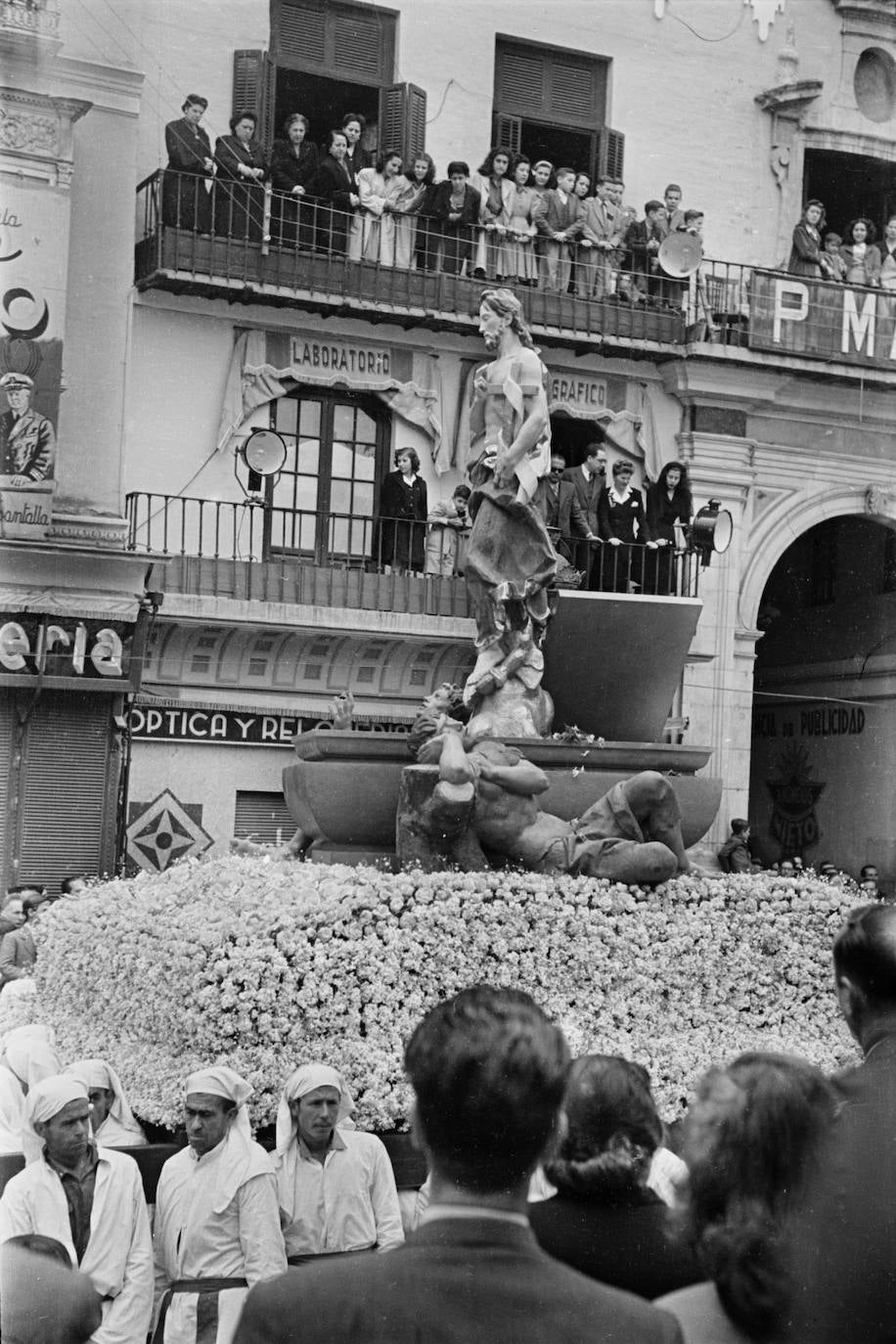 Hasta el estreno del trono realizado por Pedro Pérez Hidalgo en 1055, el grupo escultórico del Resucitado que realizó José Capuz salió en tronos confeccionados con gran cantidad de flores. La fotografía corresponde a la primera salida procesional del conjunto, en el año 1946, a su paso por la actual plaza de la Constitución.