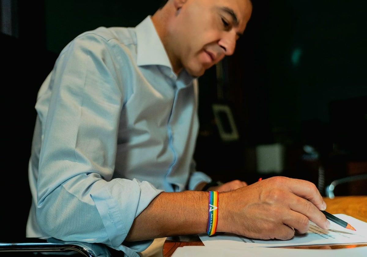 Juanma Moreno, firmando documentos en su despacho con la pulsera arcoíris