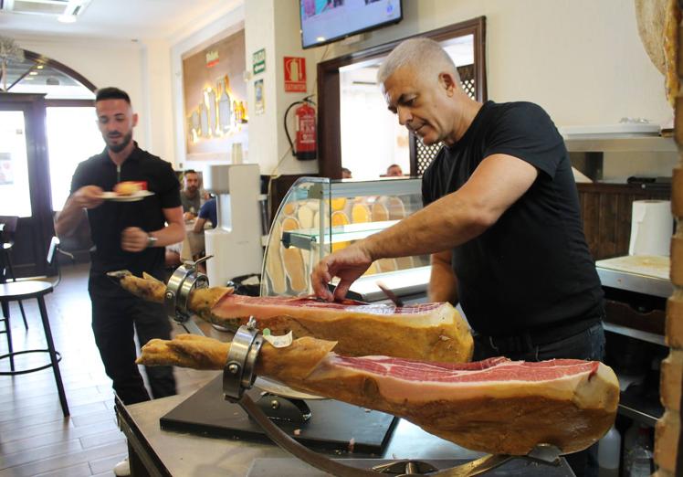 Imagen principal - Cada día Paco Zumaquero corta más de dos jamones ibéricos. Abajo, vitrina con carnes de cerdo ibérico de bellota de Salamanca y ternera de Burgos; y gazpachuelo malagueño.