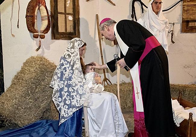 Monseñor Catalá bendice al niño que representa a Jesús recién nacido en el Belén viviente de la Casa Diocesana
