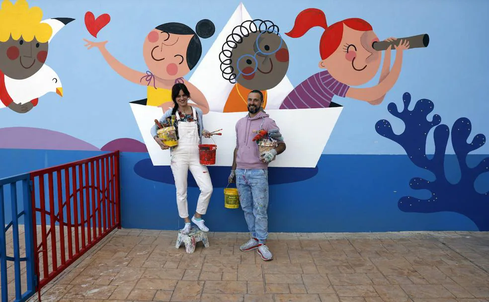 Izas y Prim, ilustradores detrás del proyecto 'Azulpatio' posan delante del mural del CEIP Carmen Martín Gaite en Rincón de la Victoria. 