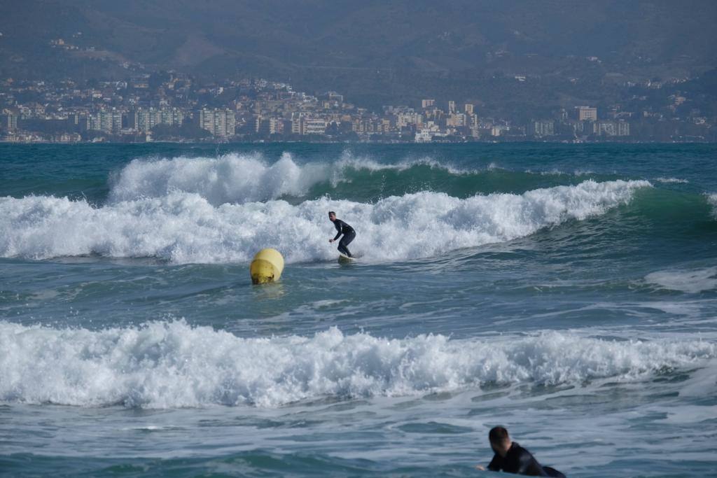 Tablas y ganas de coger olas en la playa de Huelin, este domingo. Surfistas aprovechan el viento de levante y la olas del temporal para meterse en el agua en distintos puntos de Málaga