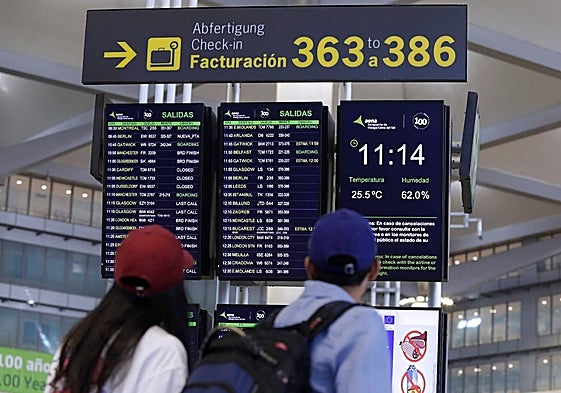 Unos jóvenes revisan sus vuelos en uno de los paneles informativos del aeropuerto.