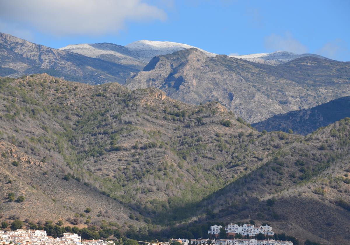 Imagen principal - Arriba, La Navachica, el 'techo' de la Sierra Almijara, cubierta con un fino manto blanco, este martes; abajo a la izquierda, La Cadena, en la Sierra Almijara, también con nieve, y a la derecha, un espectacular arcoíris, este pasado lunes en Nerja.