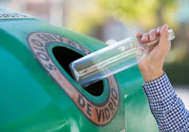 Un ciudadano deposita una botella de vidrio en el contenedor verde.