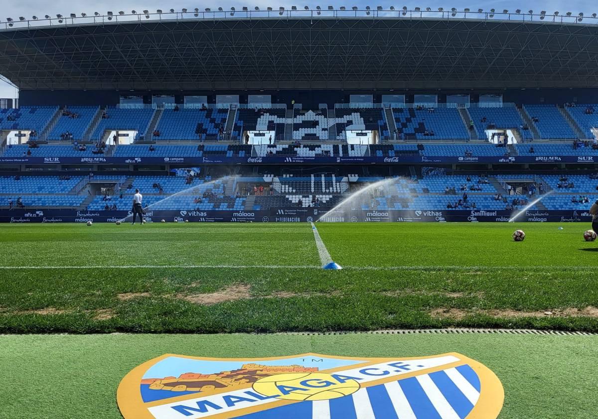 Imagen panorámica del estadio de La Rosaleda a ras de césped con el escudo del Málaga en primer plano.