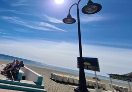 Turistas descansan junto a un puesto de hamacas, con las tumbonas apiladas, en La Carihuela.