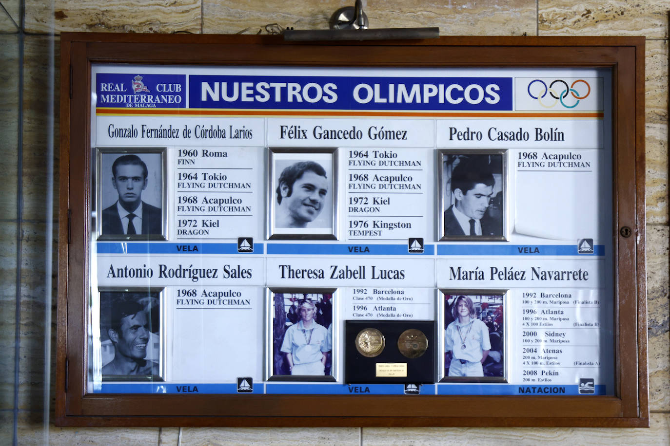 Una placa en la sala de trofeos recuerda las trayectorias de los seis deportistas olímpicos, cinco en vela y una en natación, queha tenido el Real Club Mediterráneo.