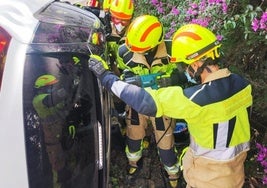 Bomberos en el lugar del siniestro, con el coche volcado.