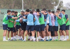 Jugadores del Málaga se refrescan durante el entrenamiento de este lunes en La Academia, con el edificio principal de la ciudad deportiva de fondo.