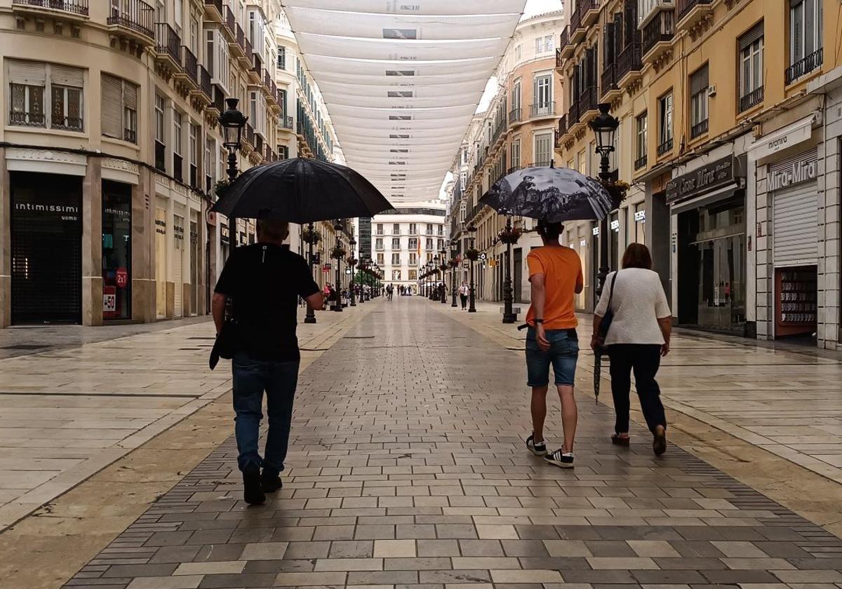 Personas caminan por una casi desierta calle Larios en un reciente día de lluvia.