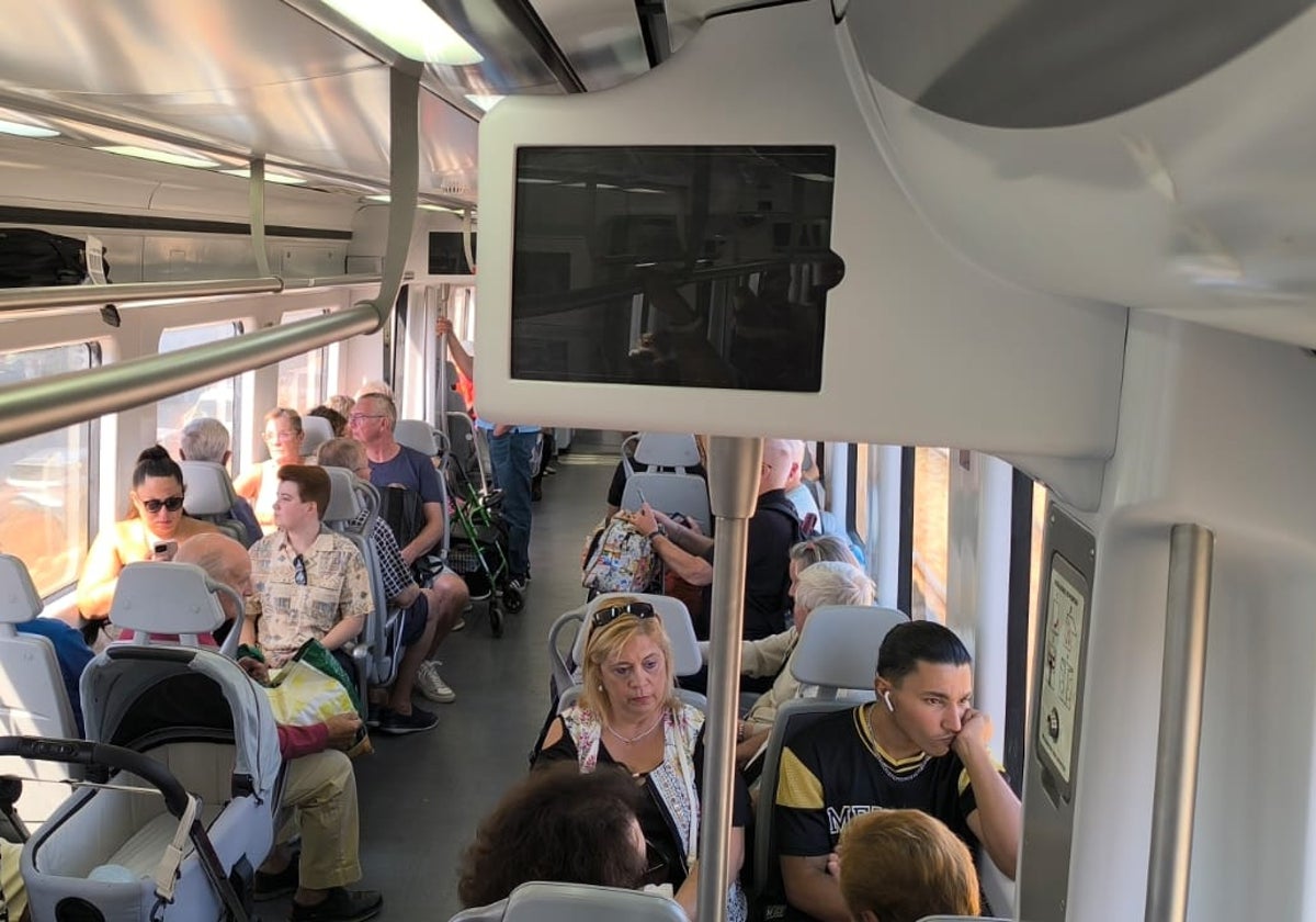 Viajeros en un tren de Cercanías de la Costa con las pantallas informativas apagadas.