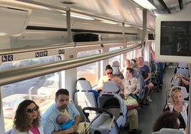 Viajeros en un tren de Cercanías de la Costa con las pantallas informativas apagadas.