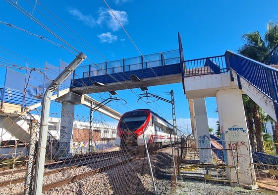 Un tren pasa debajo de la pasarela, en muy mal estado.