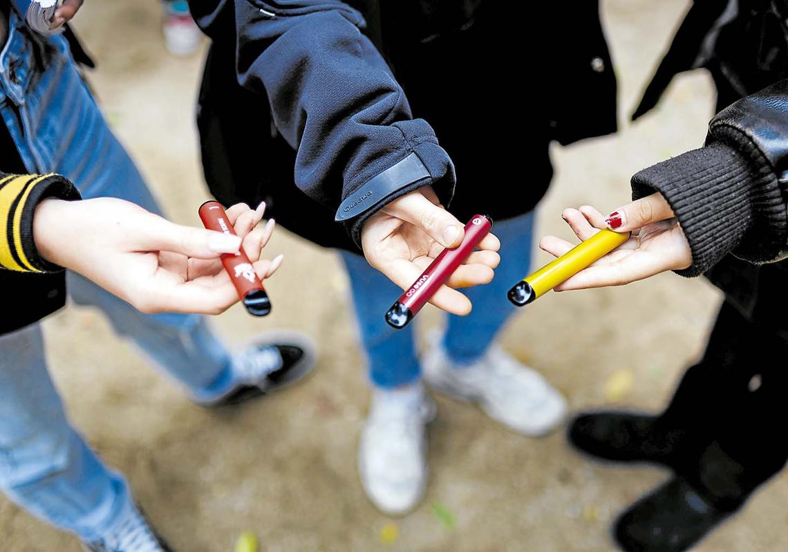 Adolescentes muestran sus vápers en la puerta de un instituto.