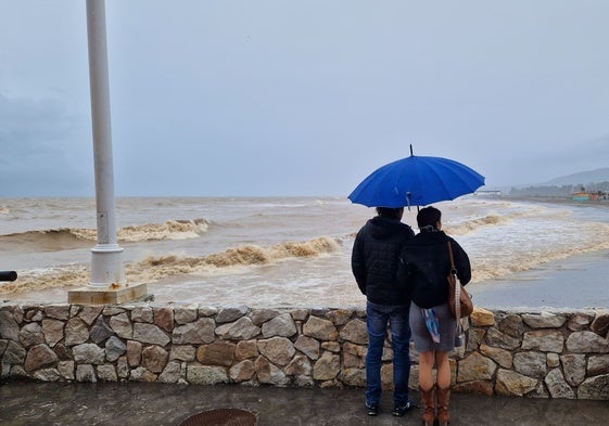 Dos personas observan el color marrón del agua del mar en Guadalmar.