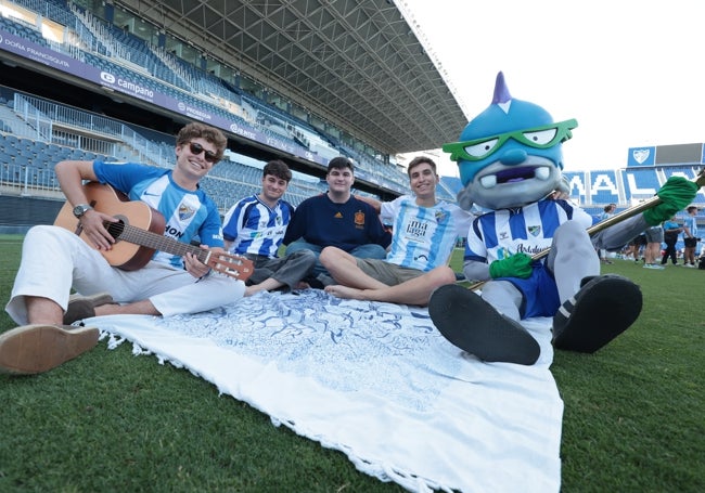 Aficionados blanquiazules, sentados con Súper Boke, la mascota oficial del Málaga.