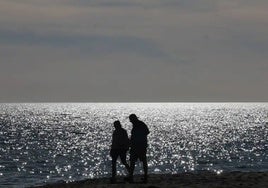 Dos personas pasean por la orilla al anochecer.