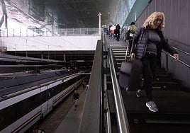 Una viajera baja por las escaleras en la estación, a pie con la maleta a cuestas.