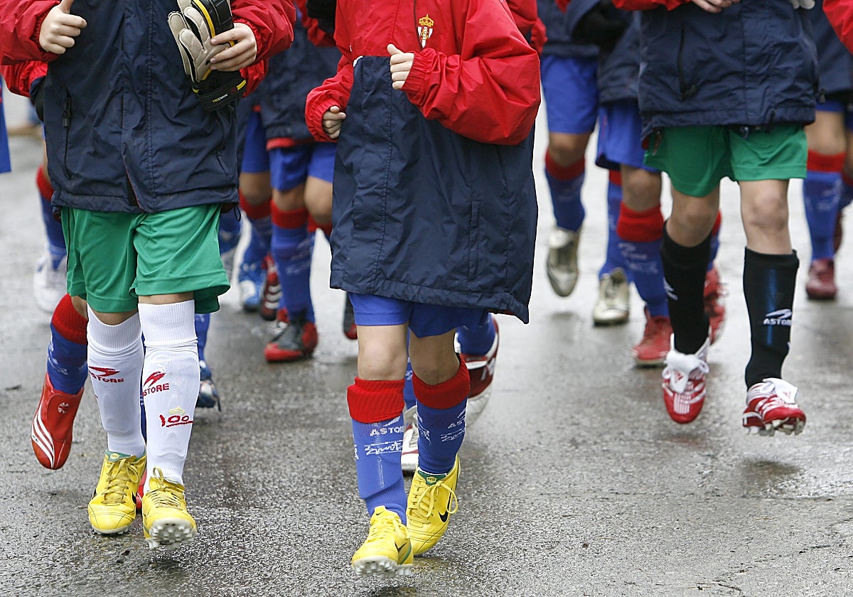 Unos niños pasean con botas de fútbol.