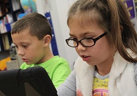 Dos niños observan atentos pantallas de dispositivos electrónicos.