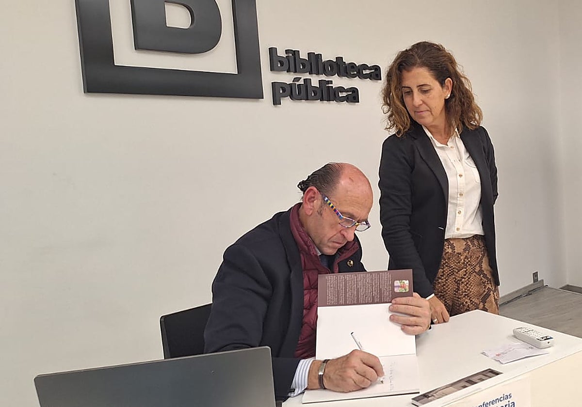 Carlos San Millán, cronista de Alhaurín de la Torre firma un ejemplar de su libro, en presencia de directora de la Biblioteca Municipal 'Antonio Garrido Moraga', Rocío Serrán.