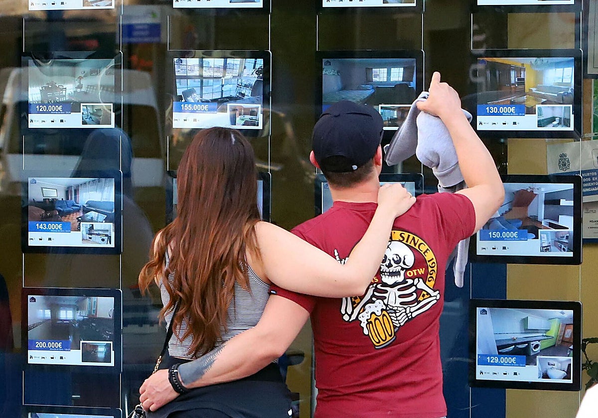 Una pareja observa las viviendas anunciadas en el escaparate de una inmobiliaria.
