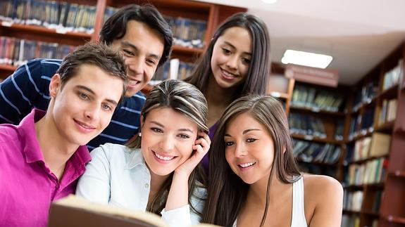 Grupo de jóvenes universitarios consulta un libro en una biblioteca