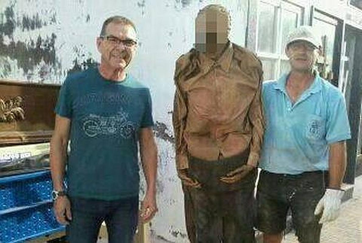 Un familiar (izq.) y el trabajador (dcha.) posan en la fotografía con el cadáver. 
