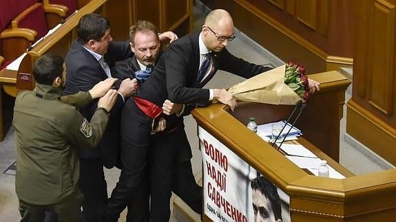 Un diputado no identificado (2º dcha.) intenta alejar al primer ministro ucraniano, Arseniy Yatsenyuk (dcha), del estrado.