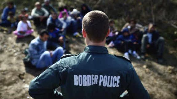 Un agente de policía de fronteras vigilando a un grupo de refugiados sirios en la frontera.