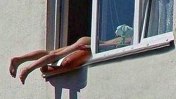 La joven toma el sol desnuda en su ventana.