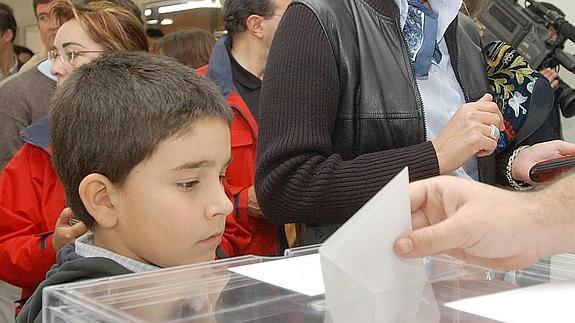Un niño observa cómo introducen un sobre en la urna.