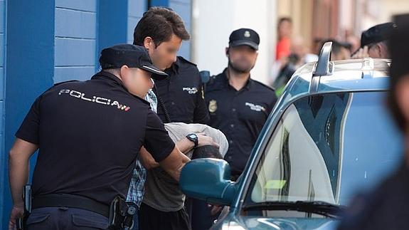 Agentes de la Policía Nacional introducen al detenido en un vehículo camuflado tras finalizar el registro en su vivienda. 